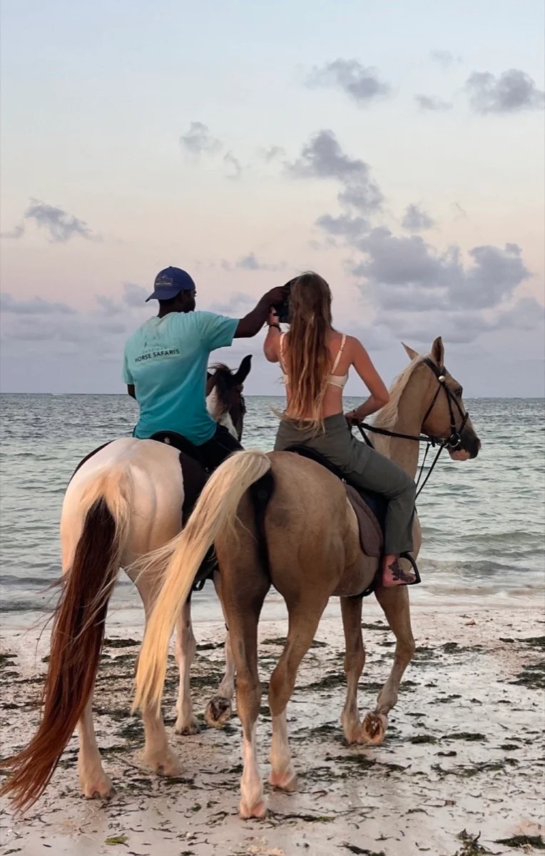 A local guide and traveler riding horses along the Zanzibar shoreline at dusk