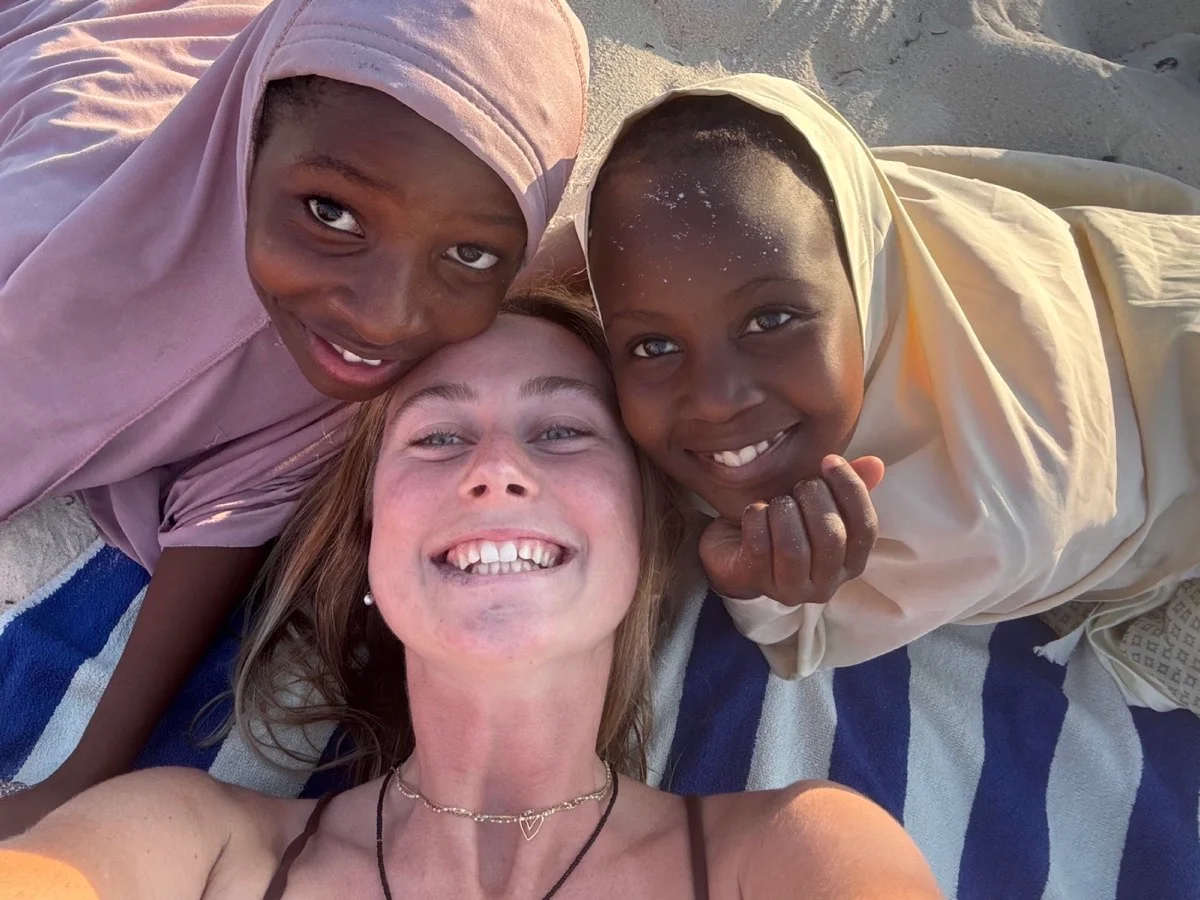 A traveler and two smiling local girls sharing a selfie on a Zanzibar beach