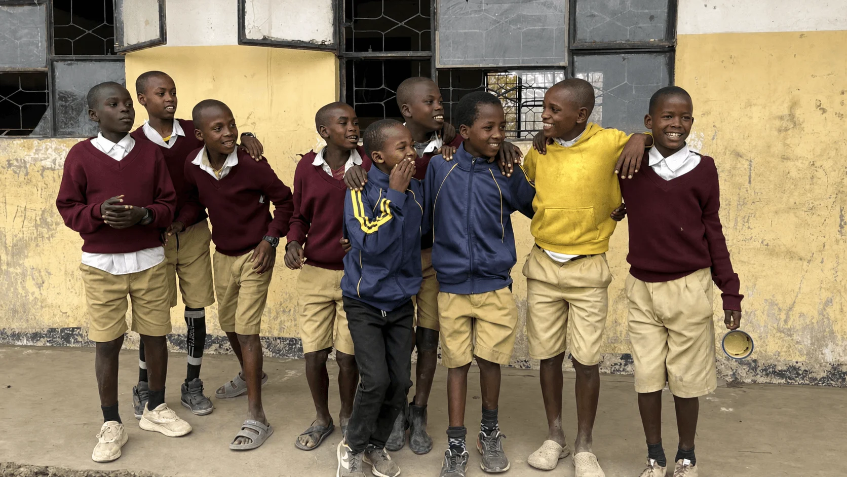 A joyful group of Tanzanian schoolchildren standing together outside their classroom