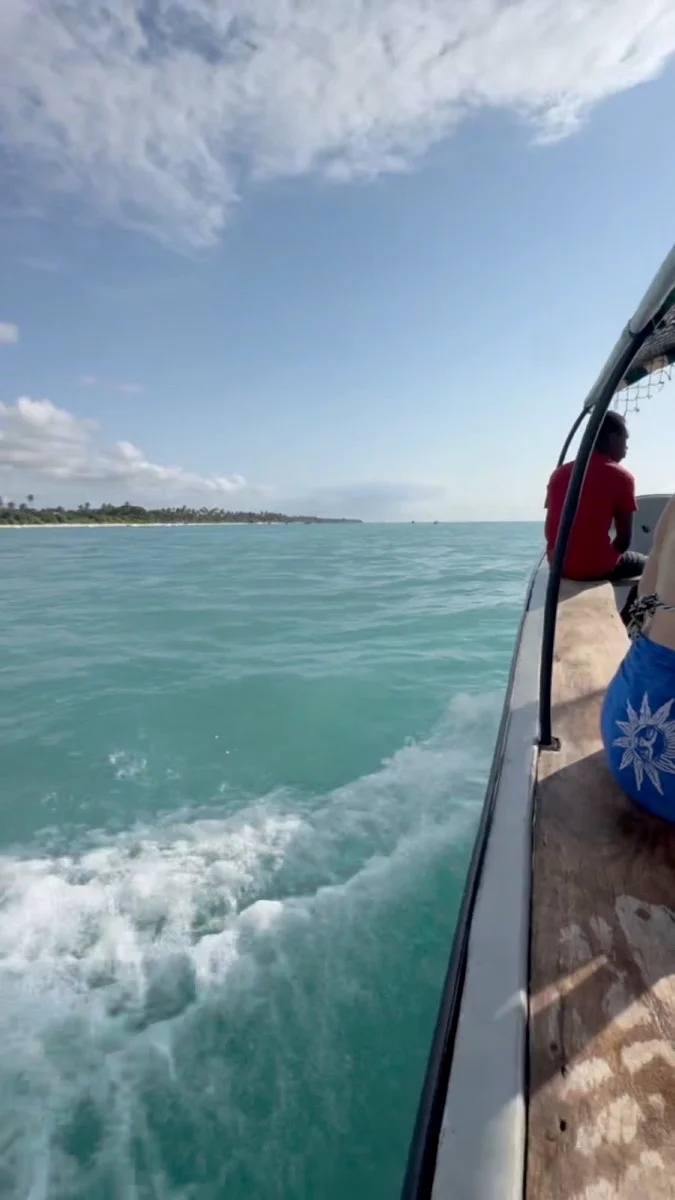 A small motorboat crossing turquoise water toward the Zanzibar coast